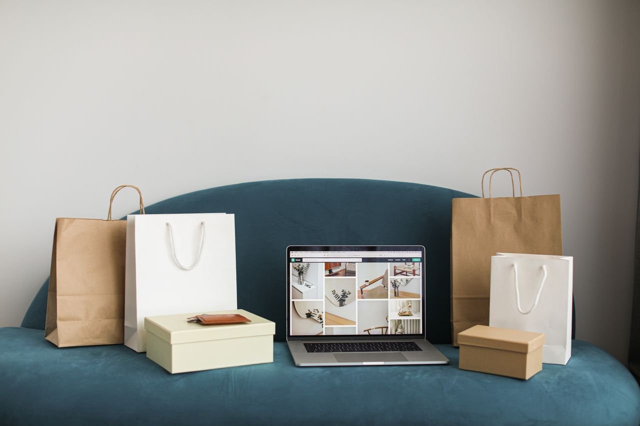 gallery-1 A laptop surrounded by shopping bags and boxes on a blue sofa, ideal for online shopping themes.